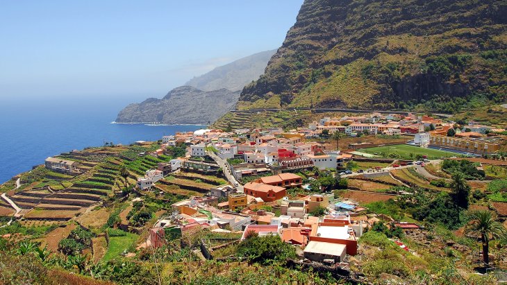 Vista panorámica de Agulo con sus tejados rojos entre acantilados y el mar, con el Teide al fondo, en La Gomera