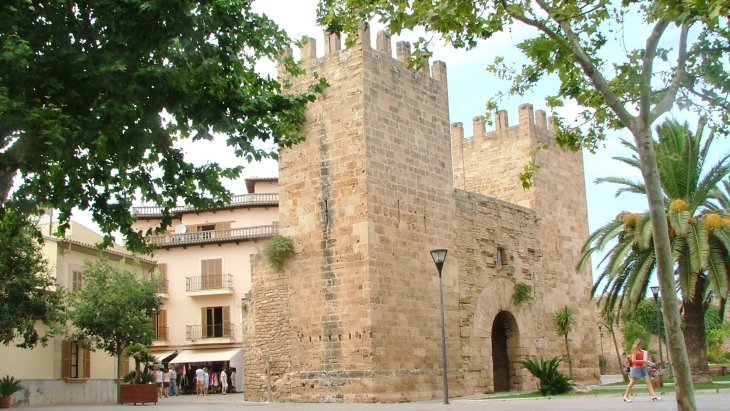 Murallas medievales de Alcúdia al atardecer, con la Porta de Mallorca y los tejados del casco antiguo del pueblo mallorquín