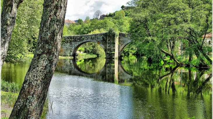 Casco histórico de Allariz junto al río Arnoia, con el puente y las casas de piedra reflejadas en el agua
