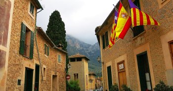 Panorámica del pueblo de Deià en Mallorca, con sus casas de piedra ocre en una colina coronada por la iglesia y montañas al fondo