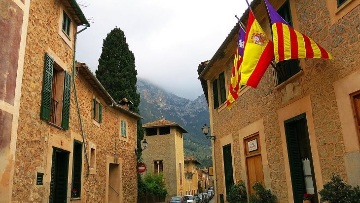 Panorámica del pueblo de Deià en Mallorca, con sus casas de piedra ocre en una colina coronada por la iglesia y montañas al fondo
