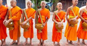 Monjes budistas con túnicas naranjas ante un templo dorado de Luang Prabang