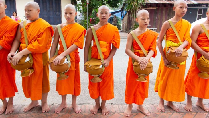 Monjes budistas con túnicas naranjas ante un templo dorado de Luang Prabang