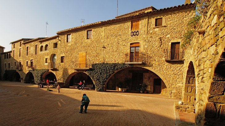 Plaza porticada medieval de Monells con arcos de piedra y casas doradas del Baix Empordà