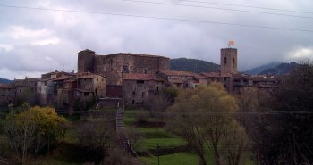 Vista del pueblo medieval de Santa Pau con su castillo y campanario entre los paisajes volcánicos de la Garrotxa