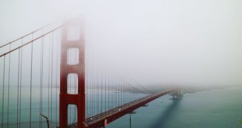 Gran puente colgante sobre el agua envuelto parcialmente en niebla