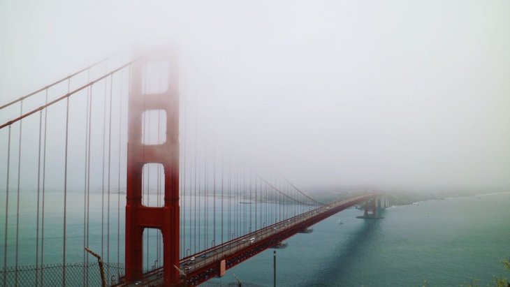 Gran puente colgante sobre el agua envuelto parcialmente en niebla
